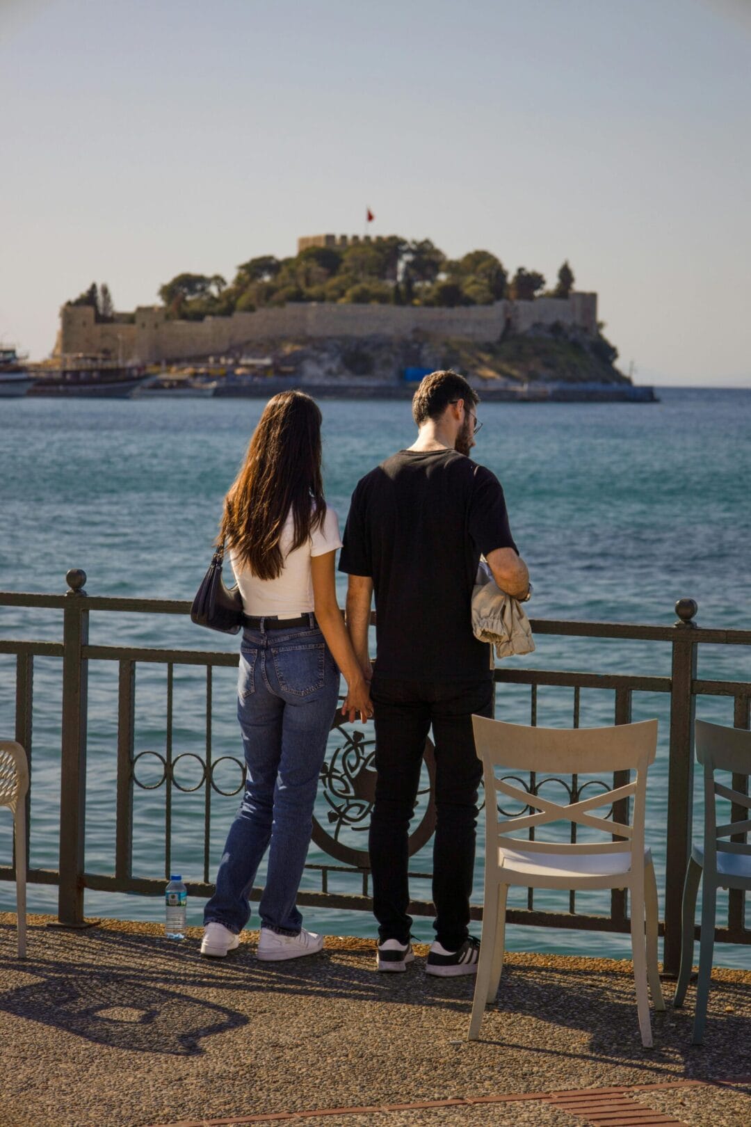 Couple holds hands by the sea with Güvercinada Island in Turkey in the background.