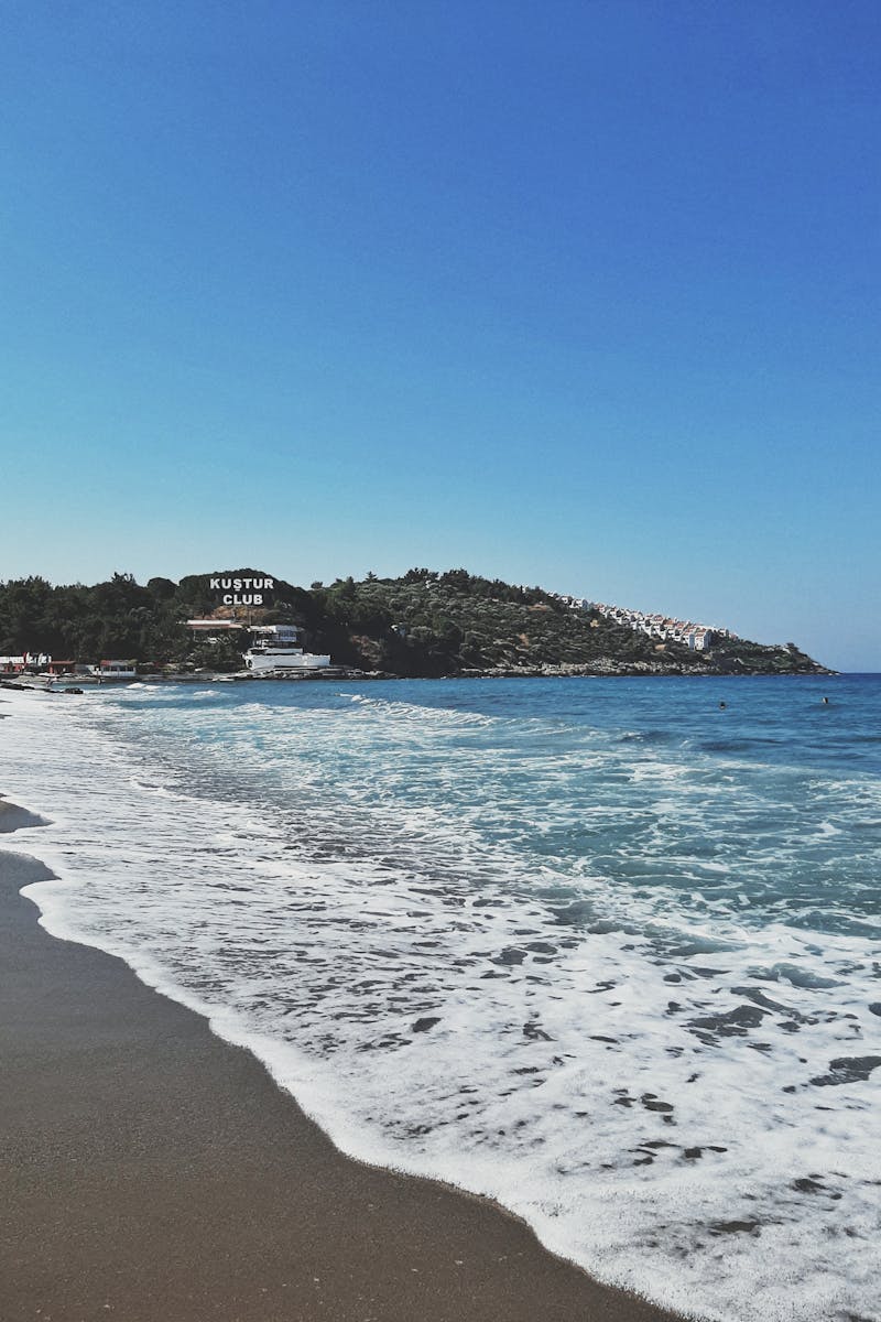 Tranquil waves crash on Kuşadası shore with clear skies in Turkey.