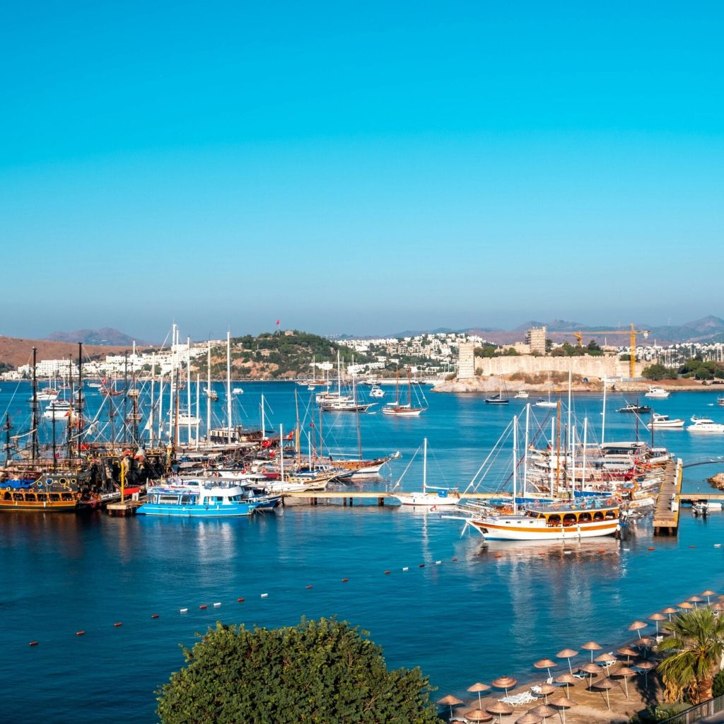 Bodrum marina with sailboats and Bodrum Castle under the sun, ideal for luxury transfers from Bodrum Airport to marina hotels and coastal resorts.