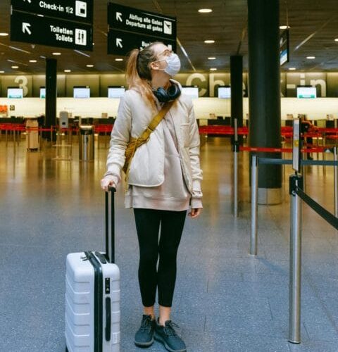 pexels-photo-3943883-3943883 A woman in a face mask stands with her luggage in an empty airport terminal.
