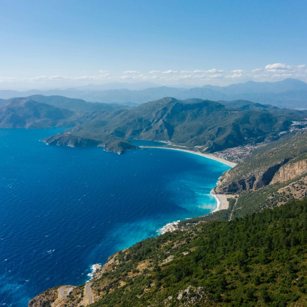 Stunning aerial shot of a coastal mountain range meeting the clear blue sea under a bright sky.